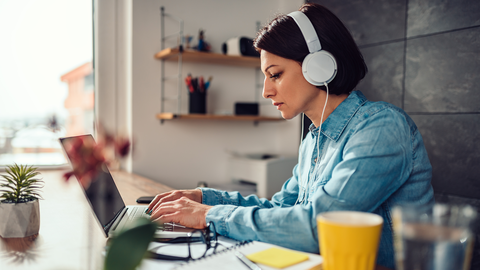 Frau mit Kopfhörer am Laptop, die sich während eines Online-Seminars Notizen macht