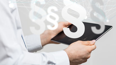 Bildkomposition mit Tablet, über das stilisierte Paragrafenzeichen gelegt sind