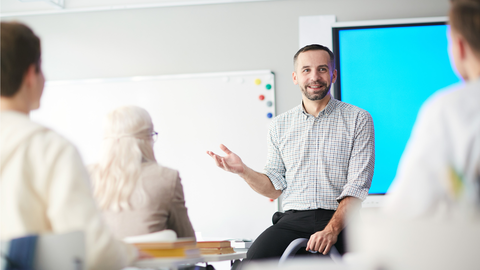Schulungssituation mit Dozent, der vor einer Anzeigentafel sitzt