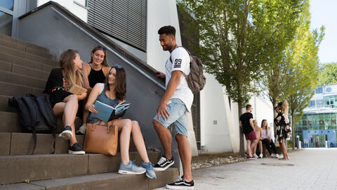Dual Studierende, die am Campus der Hochschule RheinMain auf einer Treppe sitzen