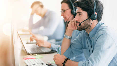 Großraumbüro, in dem drei Teammitglieder mit Headsets am Computer sitzen