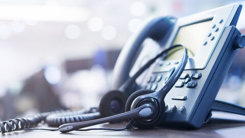 Tischtelefon mit zahlreichen Funktionstasten und daran gelegtem Headset 