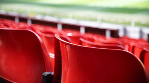 Blick über rote Stuhlreihen auf das Spielfeld eines Fußballstadiums