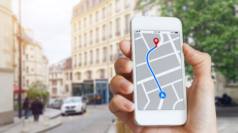 Hand mit Smartphone, das eine Straßenkarte mit Anfahrtsbeschreibung zeigt