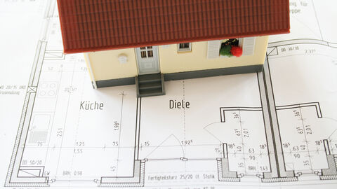 Gezeichneter Grundriss einer Wohneinheit. Auf dem Papier steht ein Miniaturhaus aus Plastik.