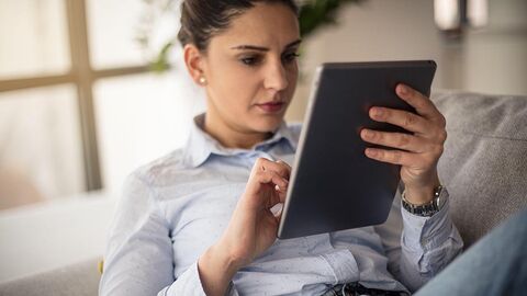 Frau in heller Bluse, die auf einem Sofa sitzend einen Text auf ihrem E-Reader liest