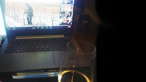 Schreibtisch mit Laptop, der einen Winzer im Weinberg zeigt, und rechts davor stehendem Weinglas