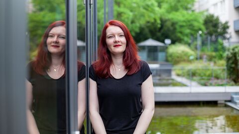 Porträt einer jungen Frau mit langen, roten Haaren und schwarzem T-Shirt im Garten des HZD-Innenhofes