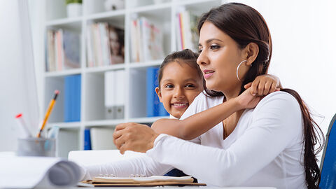 Junge Frau am Schreibtisch im Homeoffice mit Tochter im Grundschulalter 