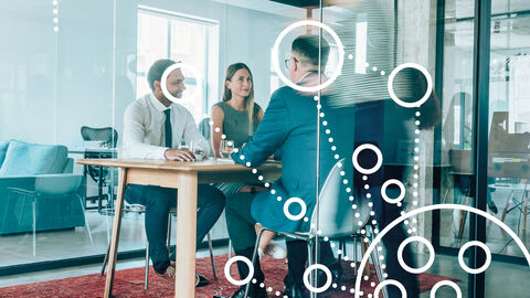 Menschen am Besprechungstisch mit darübergelegter Grafik aus Kreisen und Punkten, die ganzheitliches Projektmanagement symbolisiert