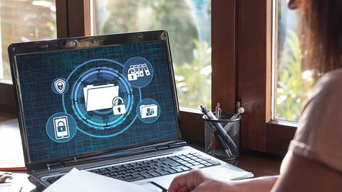 Blick auf einen Schreibtisch mit Laptop, auf dessen Bildschirm stilisierte Akten mit Schlössern zu sehen sind