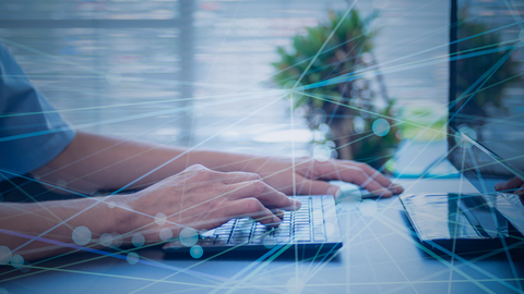 Close-up auf die Hände eines Mannes bei der Arbeit am Computer mit darüber gelegter halbtransparenter Grafik, die ein digitales Netzwerk symbolisiert