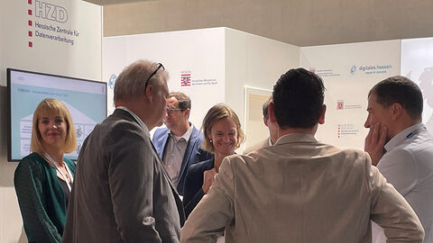 Foto des Messestands der HZD auf der SCCON22 mit Verena Schwan und Manuel Hoffrichter aus dem FISBOX®-Team im Gespräch mit Partnerinnen und Partnern aus HMdIS und HMinD