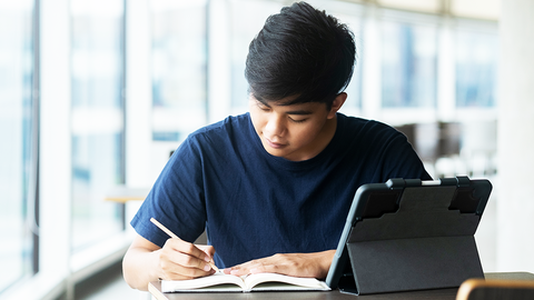 Junger Mann, der an einem Bibliothekstisch am Computer arbeitet