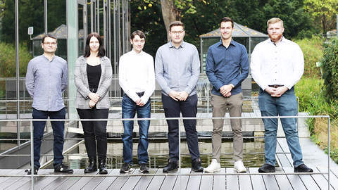 Gruppenfoto der neuen FABIs der HZD, die im Innenhof nebeneinander auf einer Holzplattform über dem Wasserbecken stehen
