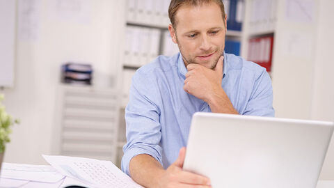 Mann vor aufgeklapptem Laptop, der Text auf dem Monitor liest