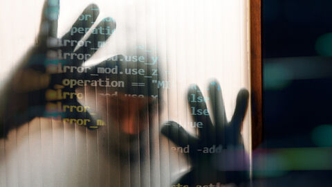 Blick durch die gerippte Glasscheibe einer Tür, auf die ein schemenhaft erkennbarer Mann beide Hände gelegt hat, darüber gelegt eine Grafik aus Programmierbefehlen