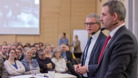 HZD-Direktor Joachim Kaiser steht mit dem Technischen Direktor Thomas Kaspar an einem Stehtisch vor Publikum. Beide sind mit Mikrofonen ausgestattet.