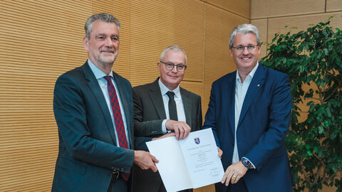 Die Staatssekretäre Dr. Martin Worms (HMdF) und Patrick Burghardt (HMinD) halten gemeinsam mit Joachim Kaiser eine Urkunde.