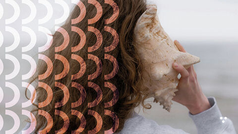 Close-up auf eine junge Frau mit langen lockigen Haaren, die eine große Muschel ans Ohr hält