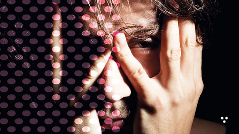 Close-up auf das Gesicht eines jungen Mannes, der beide Hände mit gespreizten Fingern um die Augenpartie gelegt hat