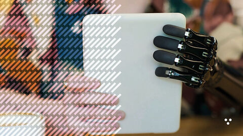 Close-up auf Mann, der mit einer schwarzen Handprothese in kruder Cyborg-Optik ein weißes Tablet hält