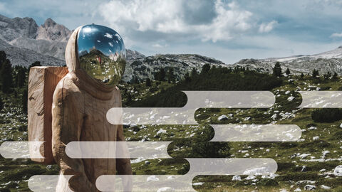 Holzskulptur eines Astronauten mit gläsernen Helm vor einer grünen Wiese mit Bergpanorama im Hintergrund