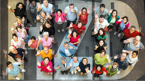 Blick von oben ins Atrium der HZD, wo bunt gekleidete Mitarbeiterinnen und Mitarbeiter die Buchstaben H, Z und D bilden