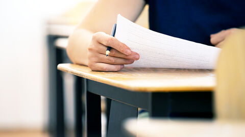 Close-up auf Person, die am Schreibtisch sitzt und einen Fragebogen in der Hand hält