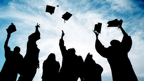 Gegenlichtaufnahme von Gruppe junger Menschen in schwarzen Roben, die Hüte in den Himmel werfen