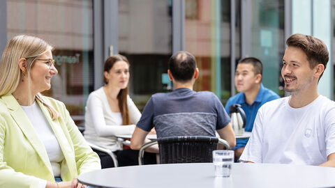 Blick in den Innenhof der HZD, wo Mitarbeitende an Bistrotischen sitzen und sich unterhalten