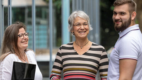 Halbtotale mit drei lachenden Mitarbeitenden der HZD im Innenhof