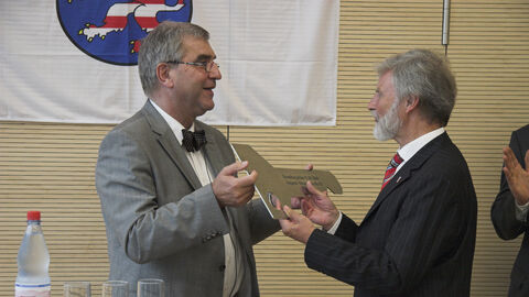 Zwei Männer stehen zusammen. Einer übergibt dem anderen einen großen Schlüssel