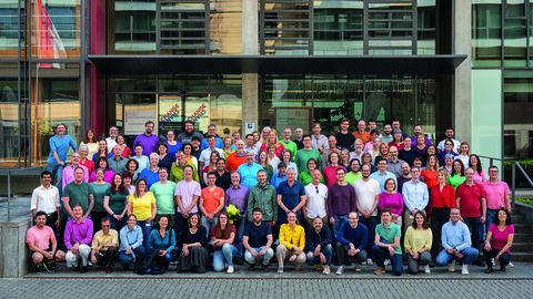 Viele Menschen stehen vor Gebäude. Alle Personen tragen etwas Buntes.