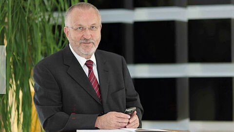 Mann im Anzug steht angelehnt an Tisch und hält Handy in Hand.