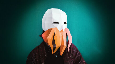 Close-up auf den Kopf einer Person, die eine Papiermaske mit weißer Haube und orangem Bart trägt