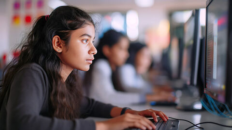 Close-up auf junges Mädchen, das neben anderen Mädchen in einer Schulklasse sitzt und aufmerksam auf einen Monitor sieht