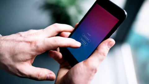 Close-up auf die Hand eines Mannes, der sich auf seinem Handy in eine App einlogt