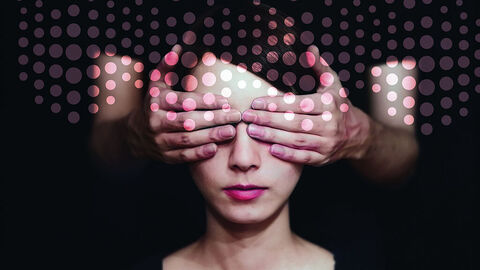 Close-up auf Gesicht einer jungen Frau, deren Augen von den Händen einer hinter ihr stehenden Personen verdeckt sind